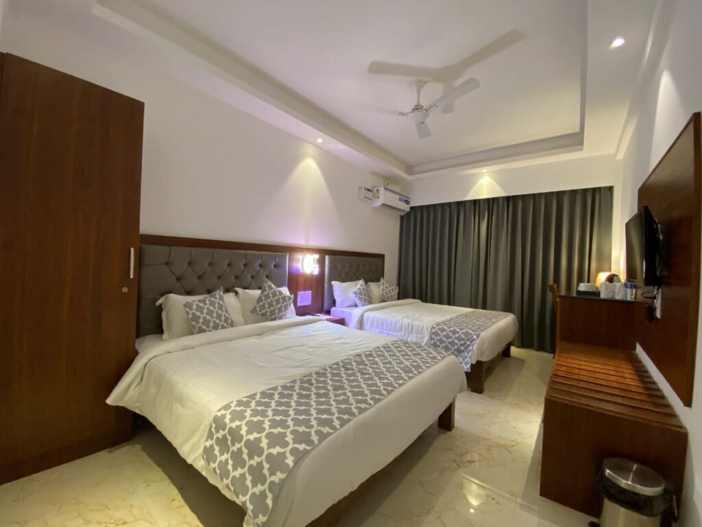 Spacious family room near Mandrem Beach Goa with two beds, air conditioning, TV, wooden furniture, and comfortable interiors
