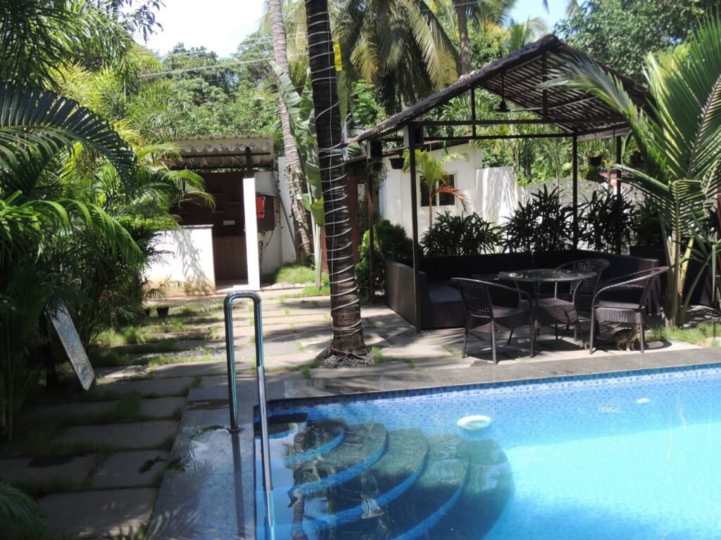 Hotel near Ashvem Beach Goa with swimming pool, tropical greenery, outdoor seating, and palm trees